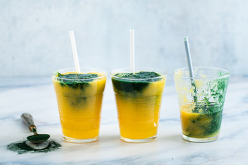 two colored fresh smoothies in glasses with fresh berries. orange banana juice with spirulina powder. detox breakfast. healthy eating