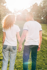 back view of young redhead couple holding hands and walking together at park