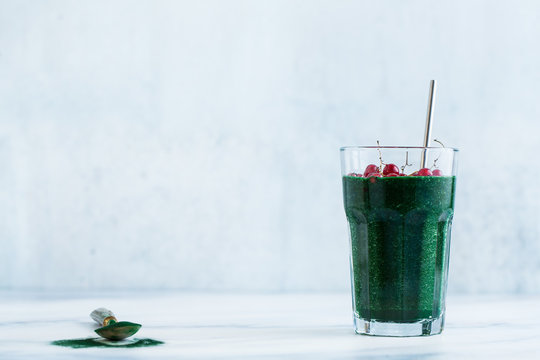a tall glass of green fruit smoothie with Hawaiian spirulina and red currant on a marble table. healthy full breakfast