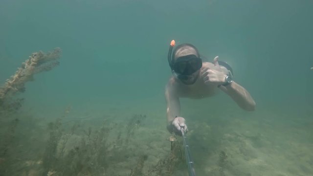 a man dives and makes a selfie under water. waving his hand to you and does like