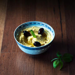  Hummus with olives and fresh herbs in a bowl on a rustic table