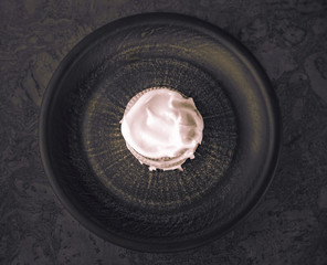 Cookies smeared with custard cream on a dark plate against a dark background, black-wite top view