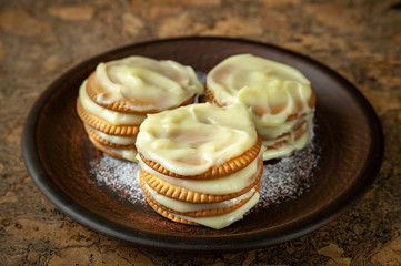 Cookies smeared with custard cream on a dark plate against a dark background