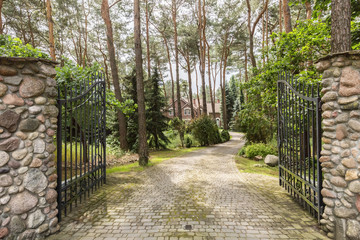 Iron entrance gate and stony road leading to the house in the woods