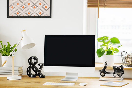 White lamp next to computer desktop on wooden desk in home office interior with plant. Real photo