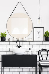 Mirror between plant and poster in white and black bathroom interior with chair. Real photo