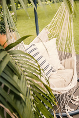 Close-up of a boho hammock hanging in a sunny garden with a palm tree and green lawn