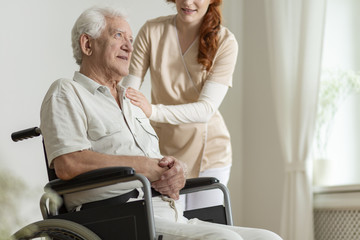 Caregiver supporting sick elderly man in the wheelchair during stay in the hospice