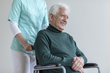 Happy senior man in the wheelchair and nurse helping him