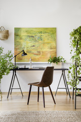 Chair at table with lamp in modern home office interior with plants and painting. Real photo