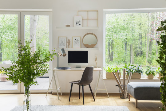Grey chair at desk with computer desktop in scandi open space interior with windows. Real photo