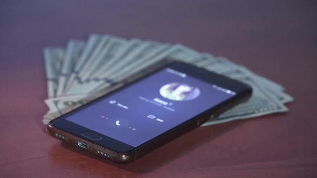 Incoming call to mobile phone on stack of green dollars