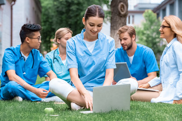 cheerful teacher and multicultural students studying outdoors with gadgets at medical university