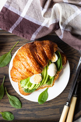 Croissant with green salad, avocado and eggs on a dark wooden tray. Breakfast, brunch or lunch concept.