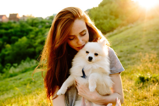 The cute red-haired woman in a hat with a spitz-dog in the park. Beautiful sunset light. Background toning for instagram filter.