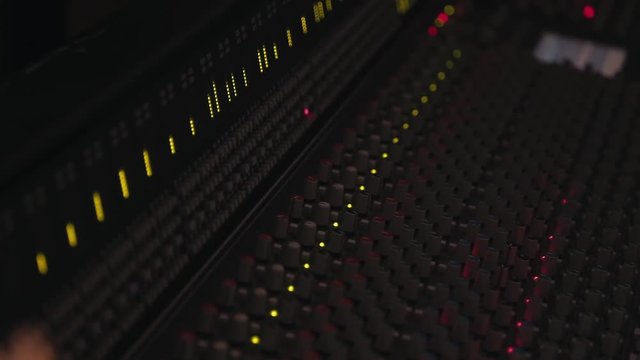 Reverse pull back across audio desk at recording studio