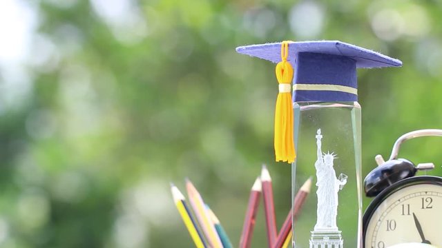 Learning study international abroad in America concept: Graduate cap on blur of USA Statue of Liberty crystal souvenir with pencils box. Idea of Work and Travel studies program