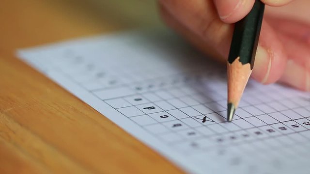 Student taking exams, writing examination on paper answer sheet optical form of standardized test on desk doing final exam in classroom, Examination sitting on row chair in school.
