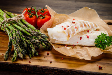 Fresh raw cod with vegetables served on cutting board on wooden table
