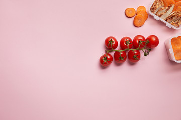 top view of fresh tomatoes and carrot slices with food containers isolated on pink