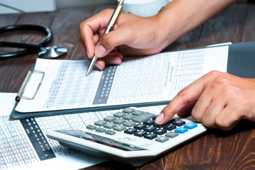 closeup of a young caucasian healthcare professional wearing a white coat calculates on an...