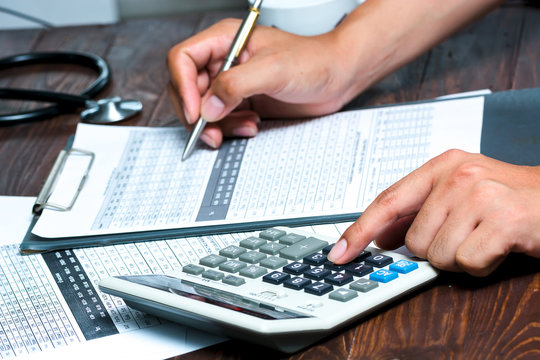 closeup of a young caucasian healthcare professional wearing a white coat calculates on an electronic calculator