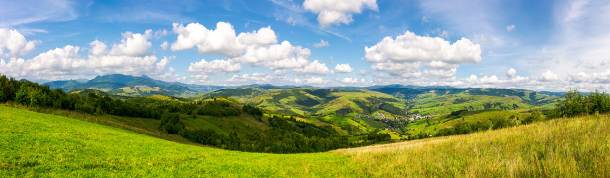 panorama of mountainous countryside. lovely countryside scenery in early autumn with grassy field on hillside, village down in the valley and clouds on a blue sky over the distant ridge