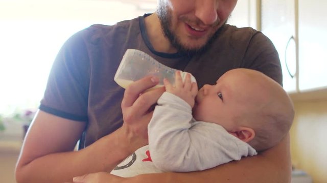Close up portrait of father and baby. A young man is feeding his three-month-old son from a bottle. Baby care, father's day