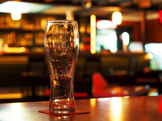 Evening. Empty beer glass on the table in a dark bar. Foam stains inside the glass