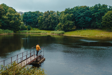 Fototapeta na wymiar Fisherman standing on pier of the lake and fishing on rainy day