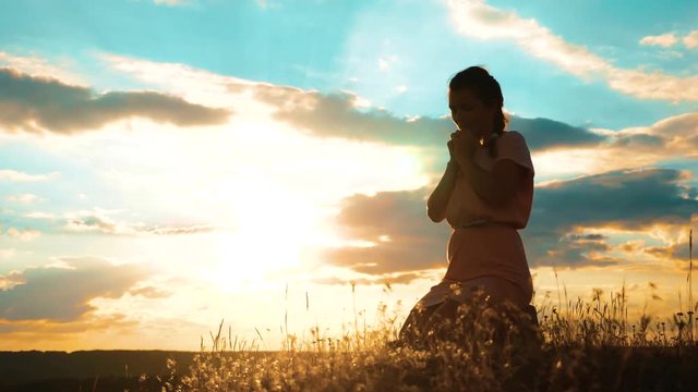 Girl lifestyle folded her hands in prayer silhouette at sunset. woman praying on her knees. slow motion video. Girl folded her hands in prayer pray to God. the girl praying asks forgiveness for sins