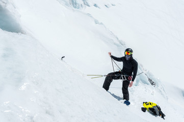 Naklejka na ściany i meble A professional mountaineer in a helmet and ski mask on the insurance does notch the ice ax in the glacier. The work of a professional climber in winter on a glacier against the blue sky