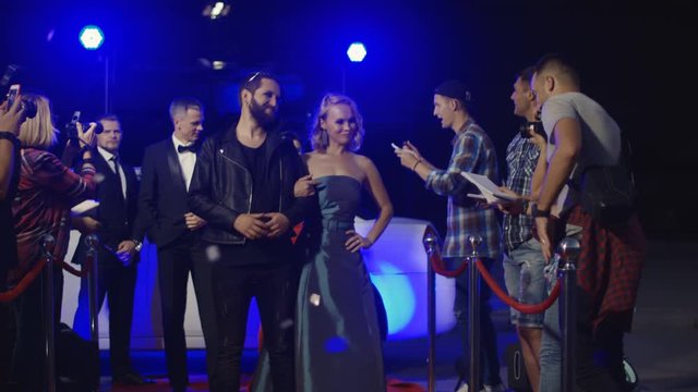 Artists arriving on celebrity event and standing on red carpet while interacting with fans and photographers