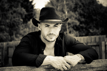 Sexy, handsome, hunky cowboy with hat open shirt and pecs looks at camera
