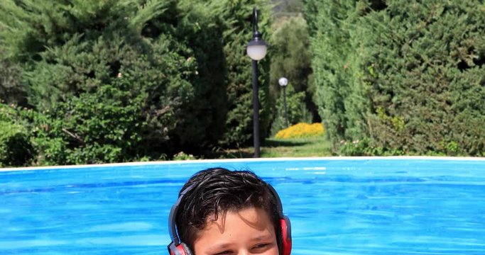 Happy preteen boy in swimming pool listening to music  with headphone and relaxing on a sunny summer day