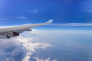 Fototapeta premium Flying into blue sky and sea of clouds and Wing of airplane with skyline top view as look from window airplane, during flight space for text message, frame or traveling idea concept