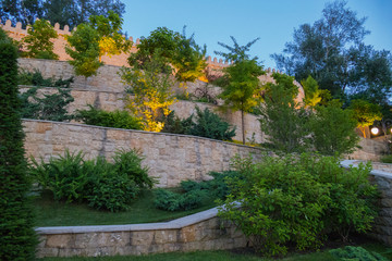 Flower beds growing on the steps of the wall going up. Some plants are illuminated from below with lights for the effect of beauty.