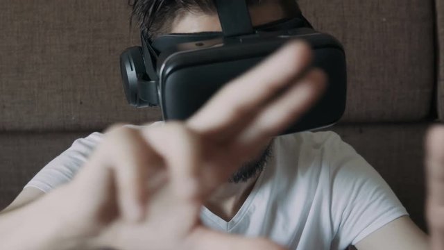 Close up shot of a young bearded man wearing virtual reality glasses - surfing net via virtual reality interface.