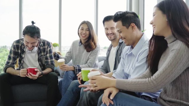 Diversity of young people group team  holding coffee cups and discussing something with smile while sitting on the couch at office. Coffee break time at creative office.