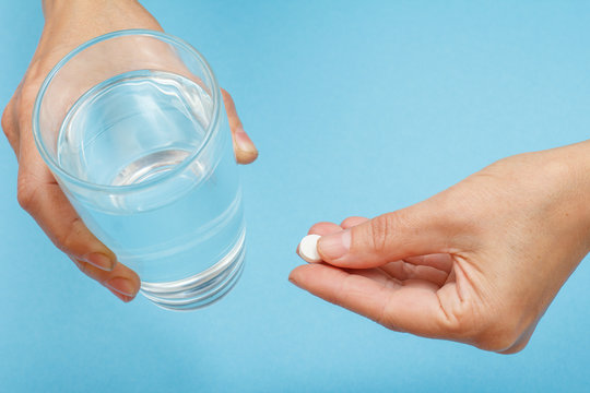 Close up hands of female patient with glass of water in one hand and white pill in another
