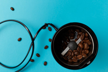 Electric coffee grinder with roasted coffee beans on the kitchen table with blue tabletop. Top view