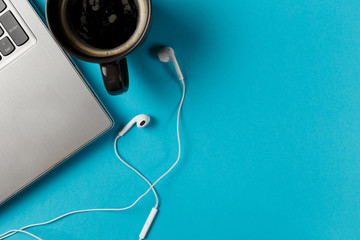 Minimal workspace with Laptop, coffee Cup and headphones copy space on blue background. Top view. Flat lay style.