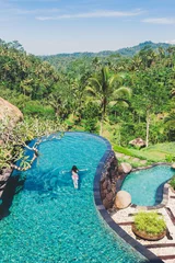 Crédence de cuisine en verre imprimé Bali La fille nage dans une grande et belle piscine sur fond de végétation tropicale luxuriante. Une jeune femme nage dans une piscine extérieure avec une belle vue sur les palmiers, Bali, Indonésie. Vue d& 39 en-haut.
