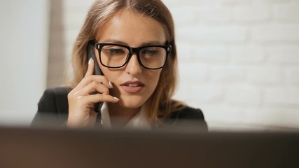 Manager doing business on phone while working at the laptop, busy smart woman dealing with customers in modern white office on typical hectic morning - Powered by Adobe