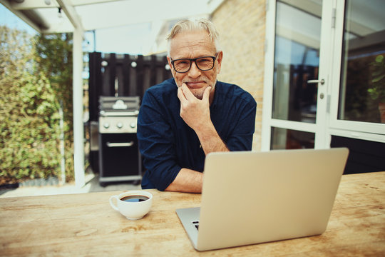 Smiling Senior Man Using A Laptop Outside On His Patio