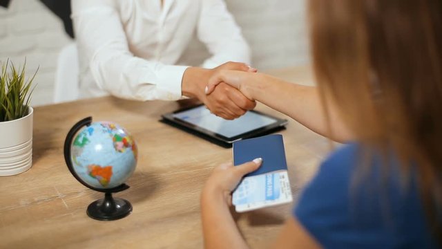 Fair-haired woman receiving documents in travel agency, getting passport and ticket on typical busy weekday, shaking hands after successfully conducted deal