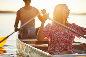 Young woman laughing while canoeing with her boyfriend in summer