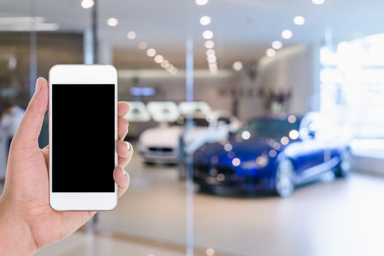 man hand using mobile smart phone with blank screen in a blurred background of car showroom