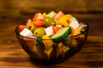 Glass bowl with greek salad on wooden table
