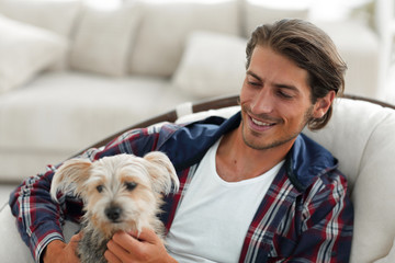 handsome guy stroking his dog while sitting in a large armchair.